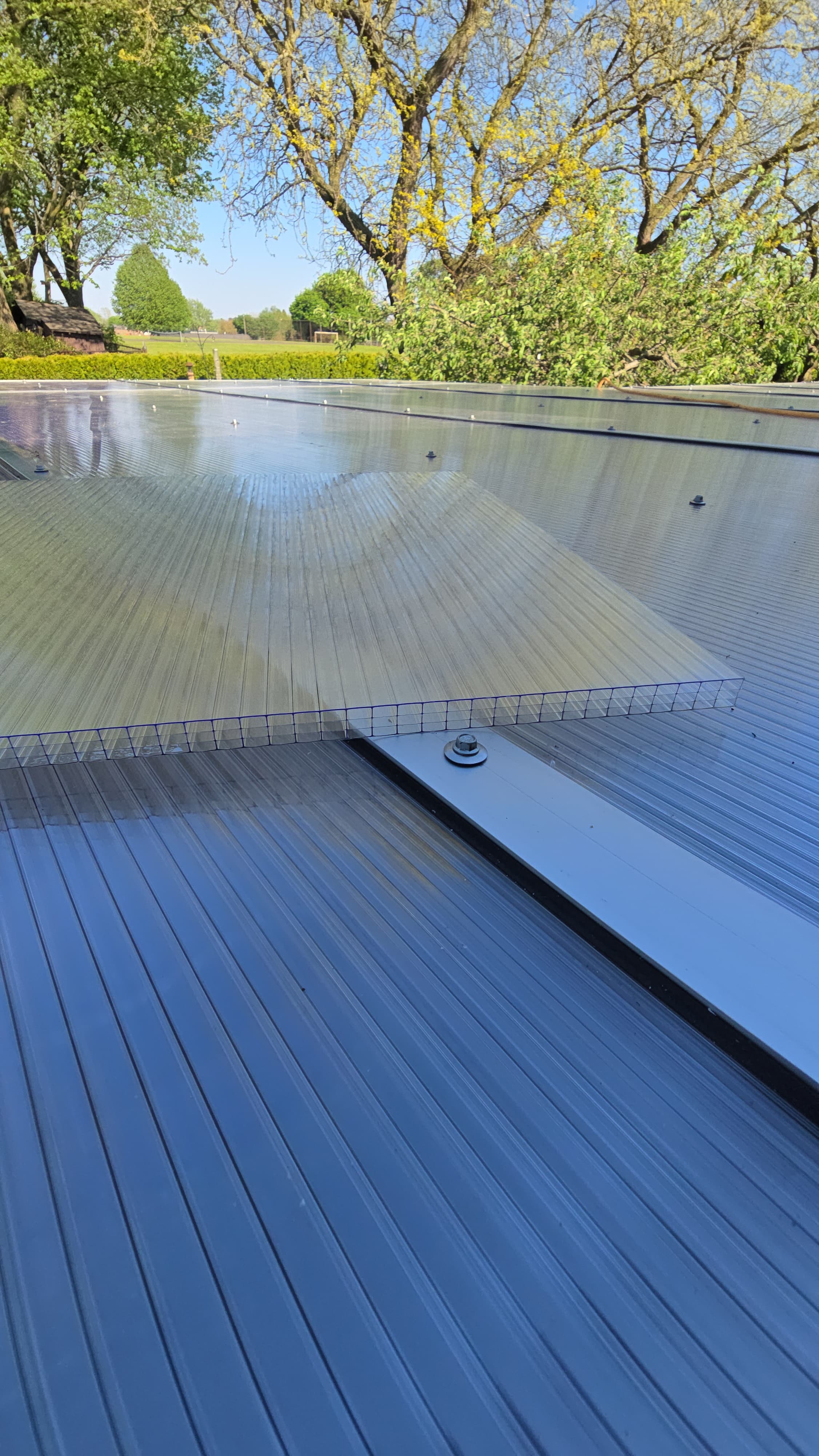 Twinwall polycarbonate panel lifted over an installed roof showing the aluminum cap and screw